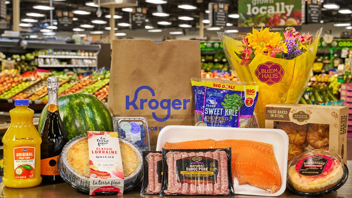 Grocery items including quiche, orange juice, a floral bouquet and sweet kale, on a table at a grocery store.