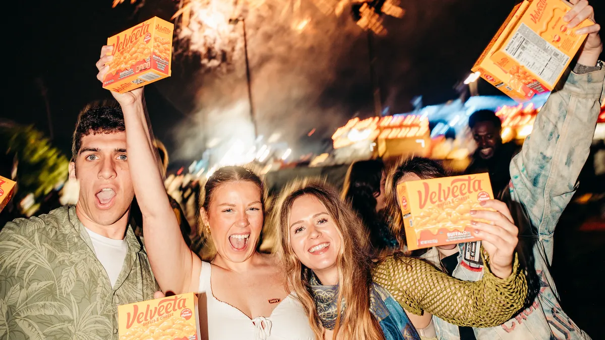 Four people holding boxes of Velveeta mac and cheese with fireworks in the background.