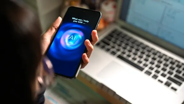 A person uses an AI chatbot on a smartphone while sitting in front of a computer