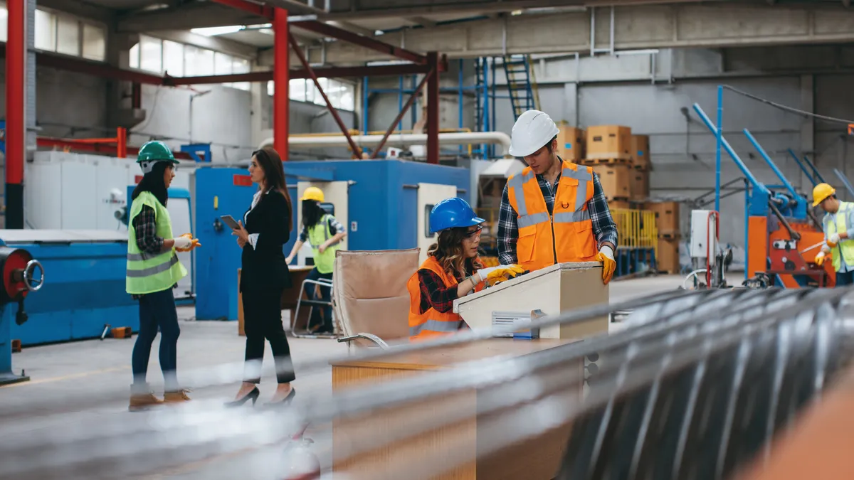 Industrial worker team wearing reflective clothing and crash helmet working in a production line at the manufacturing plant