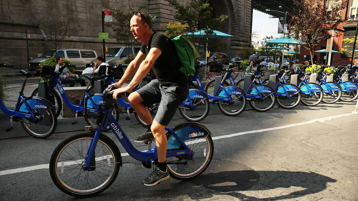 A man rides a bike along a street lined with more rental bikes.