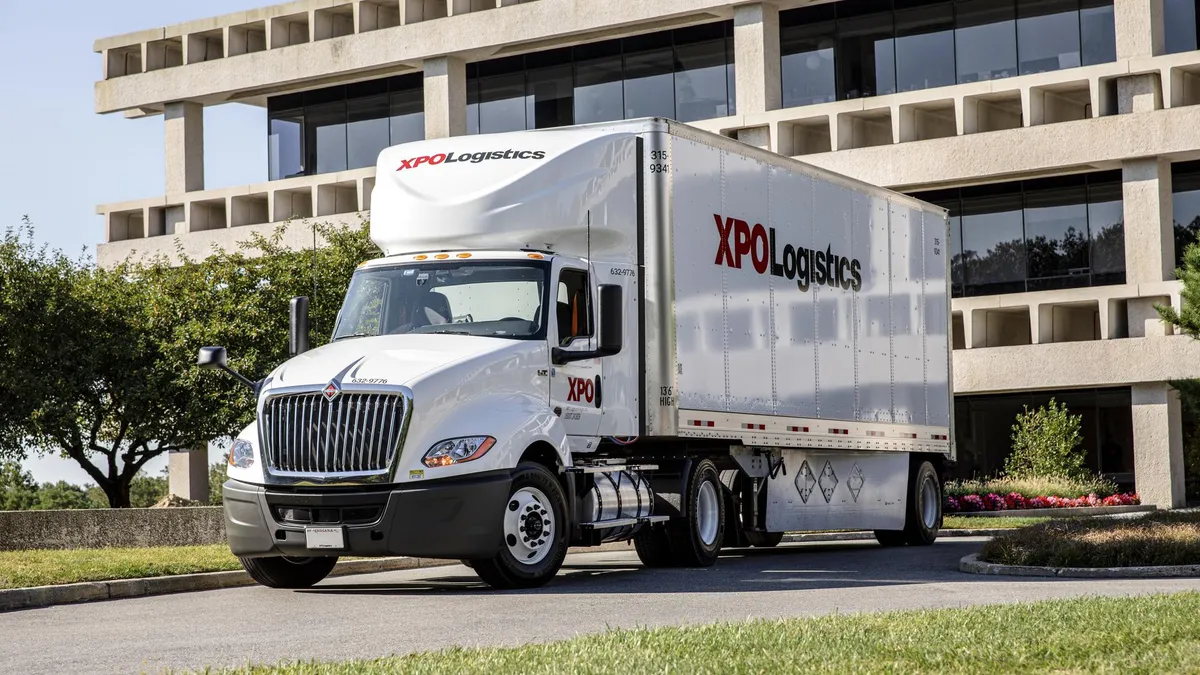 a large white truck with XPO Logistics branding in red and black outside an office park.