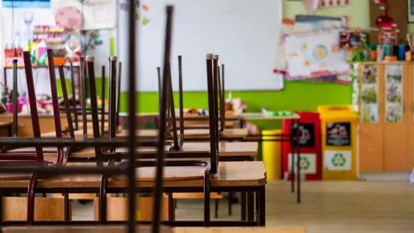 Chairs are placed on top of individual desks in an empty classroom.