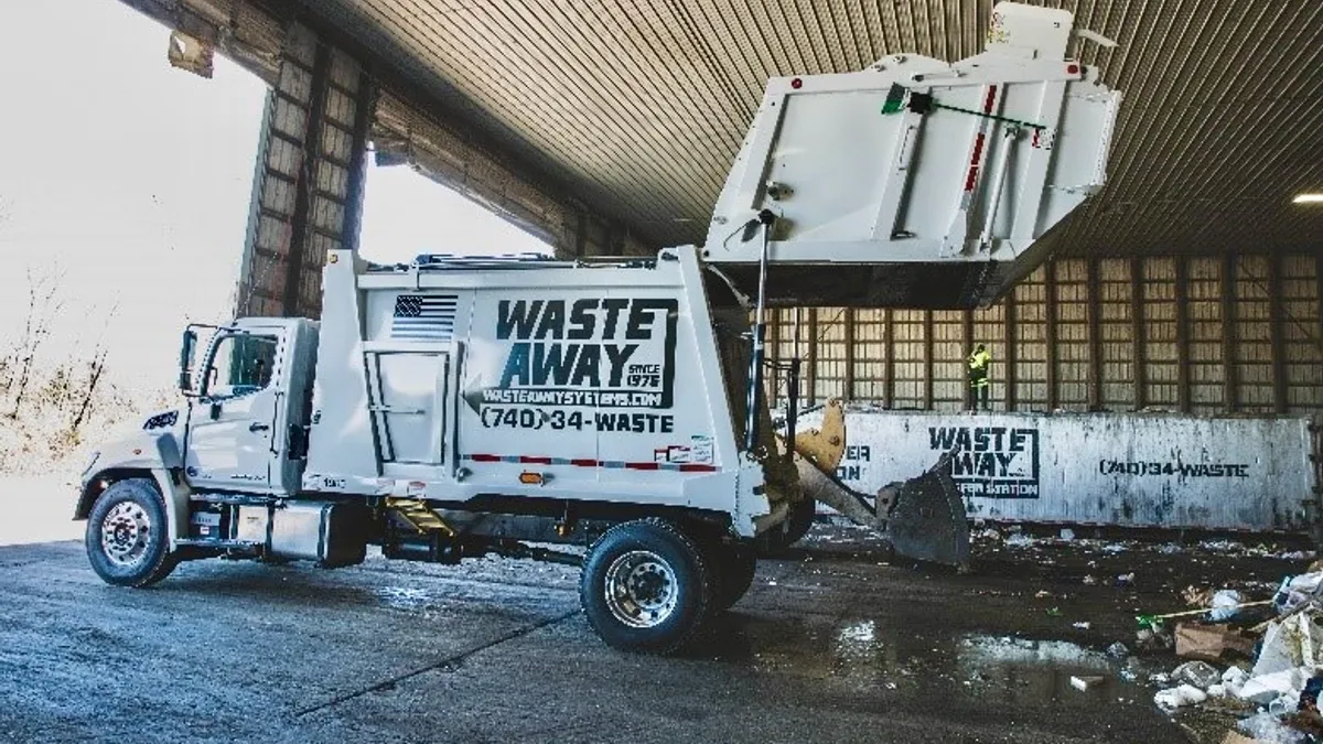 Trash truck tipping waste onto the floor of an industrial transfer building