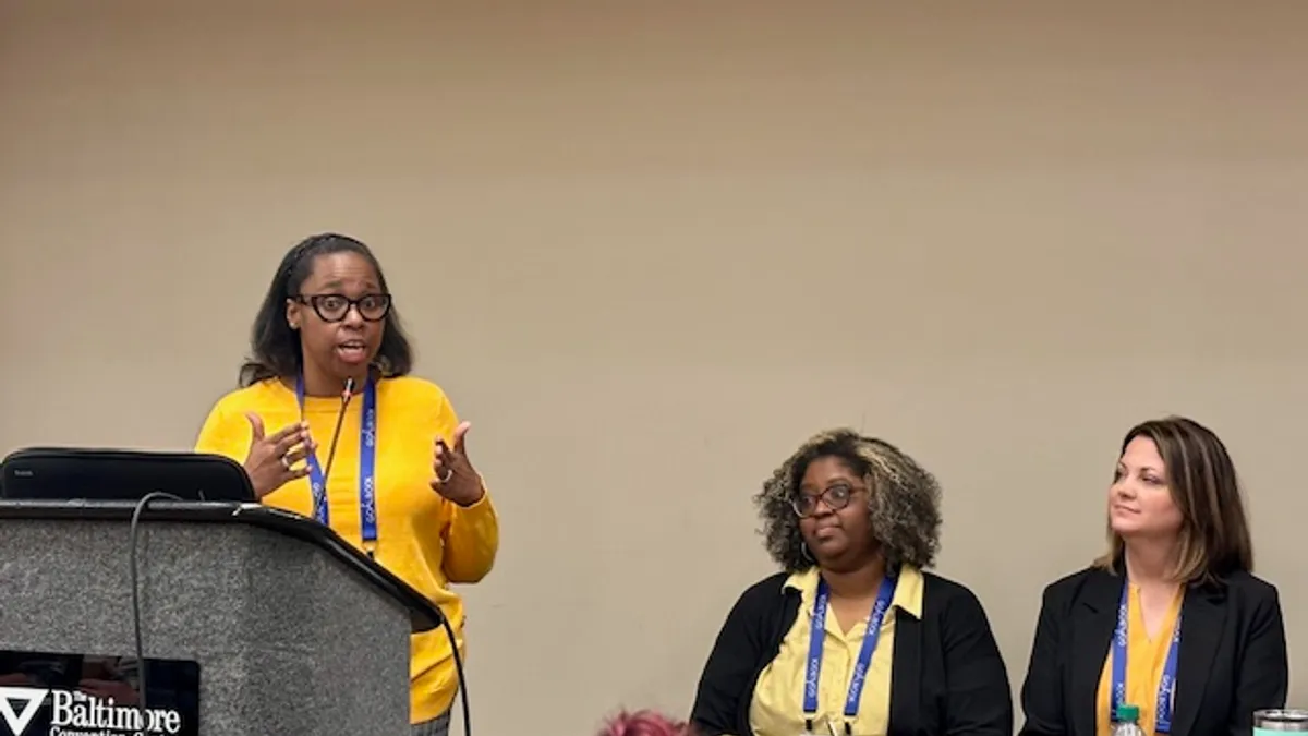 Three people are pictured with one standing behind a podium and the other two seated.