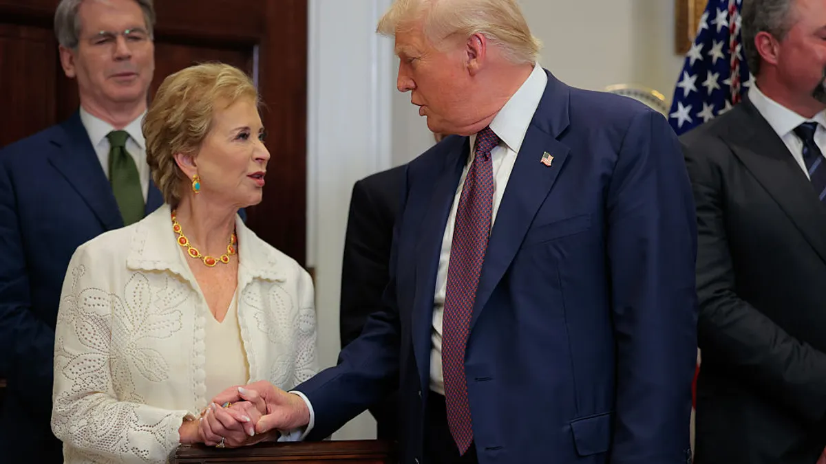 Two people are standing side by side and shaking hands inside a room.