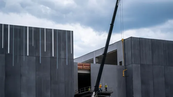 Workers in fluorescent work vests on a scaffold are dwarfed by giant data center under construction