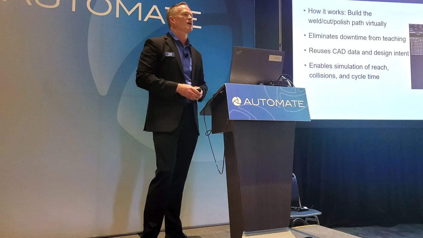 A person stands on a stage next to a podium with a blue background that says "Automate."