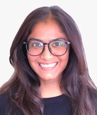 A headshot of an Indian woman with long hair and thick glasses.