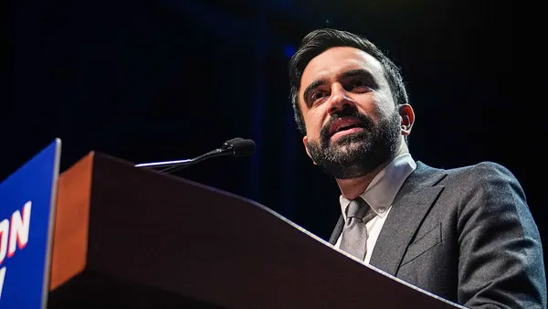 A person with a beard speaks at a podium.