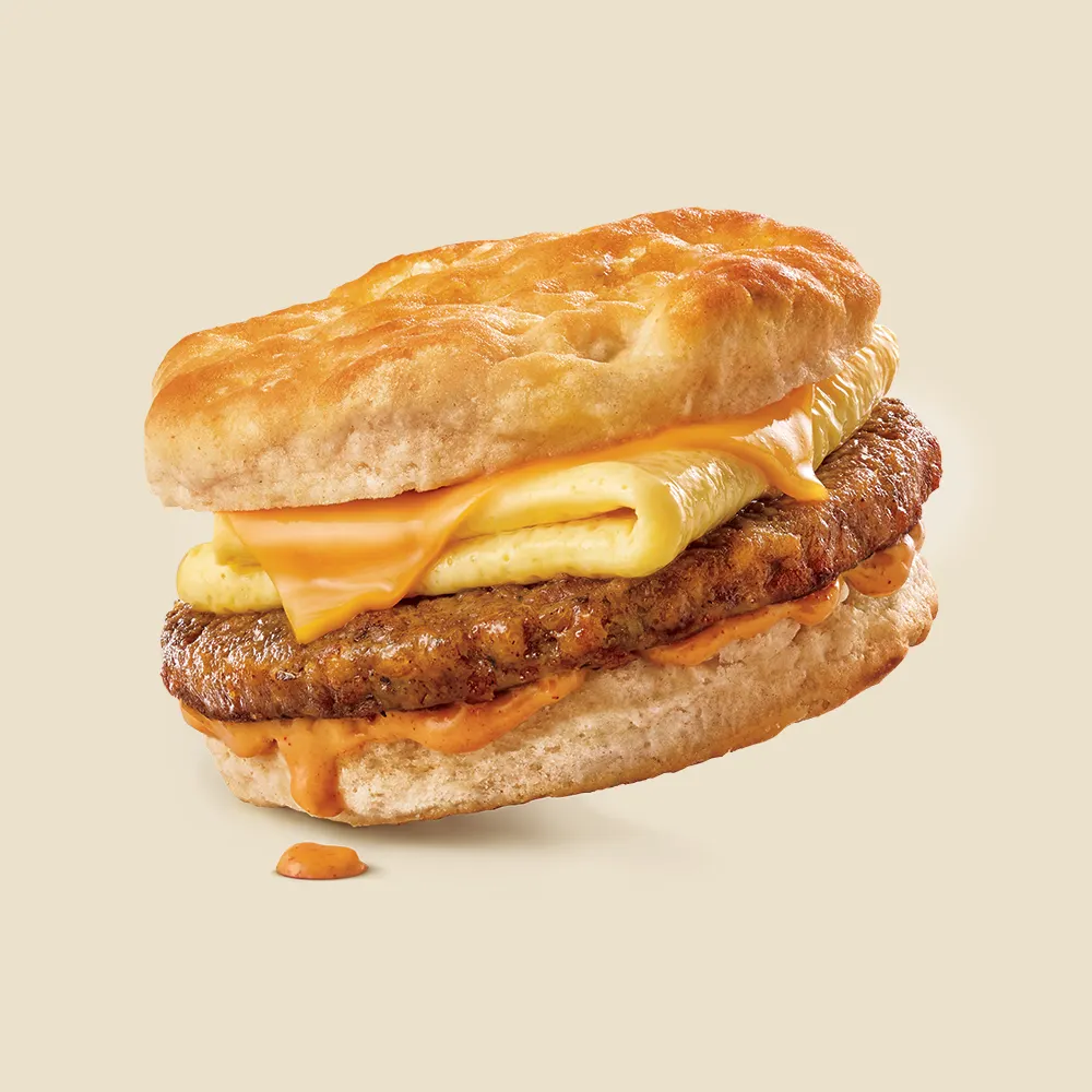 A breakfast sandwich on a biscuit with a plant-based sausage patty from Jack & Annie's, a folded egg, a slice of cheese and orange sauce.