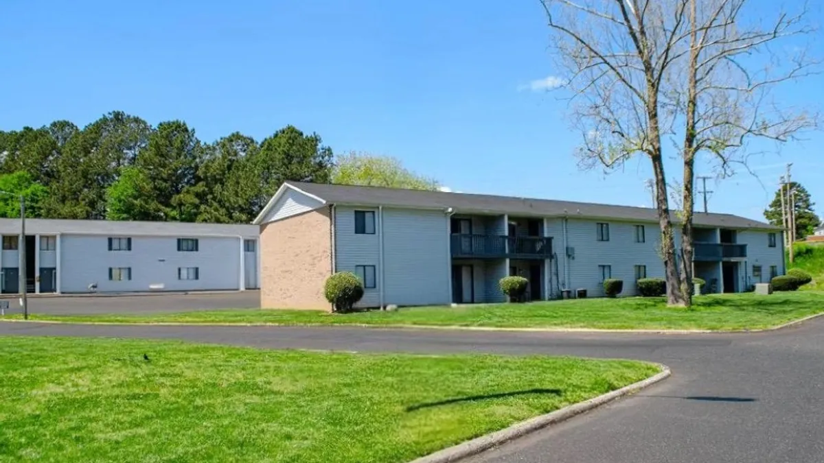 Two-story apartment building surrounded by grass and trees.