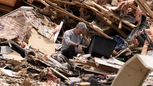 A man sits with his head in his hands in a large pile of rubble.