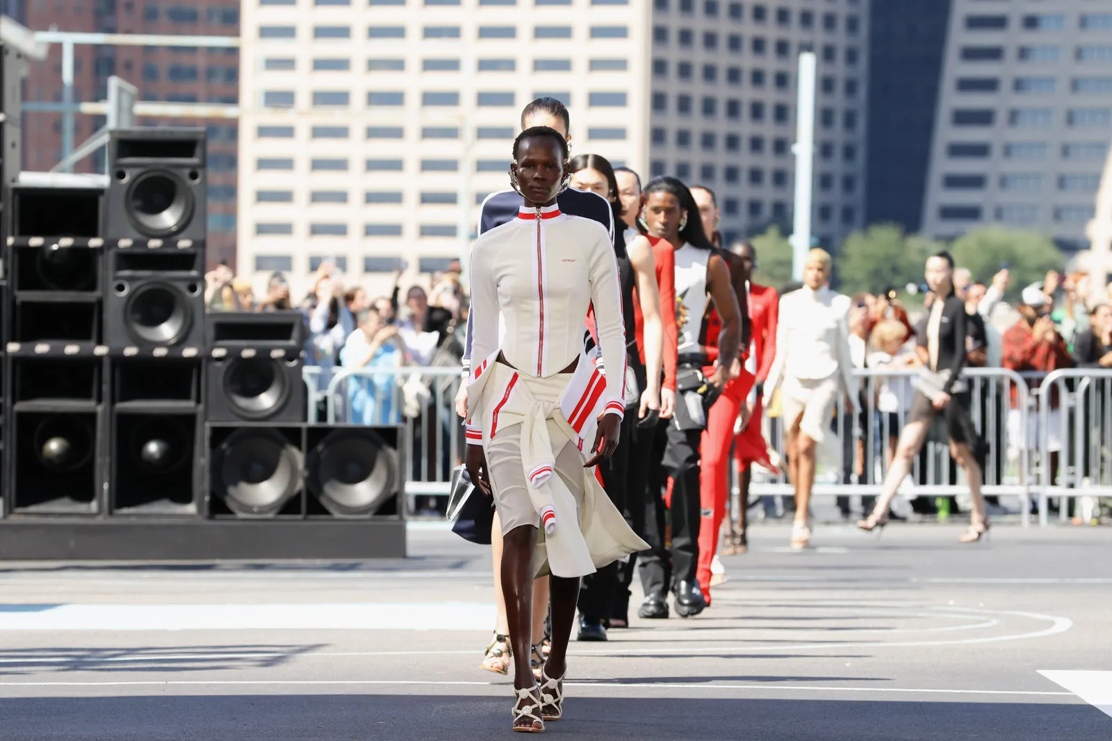 Models walk in a line wearing black, white and red clothing on a basketball court during a fashion show.