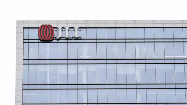 A JLL logo is adhered to the top left of a sleek glass commercial building facade. 