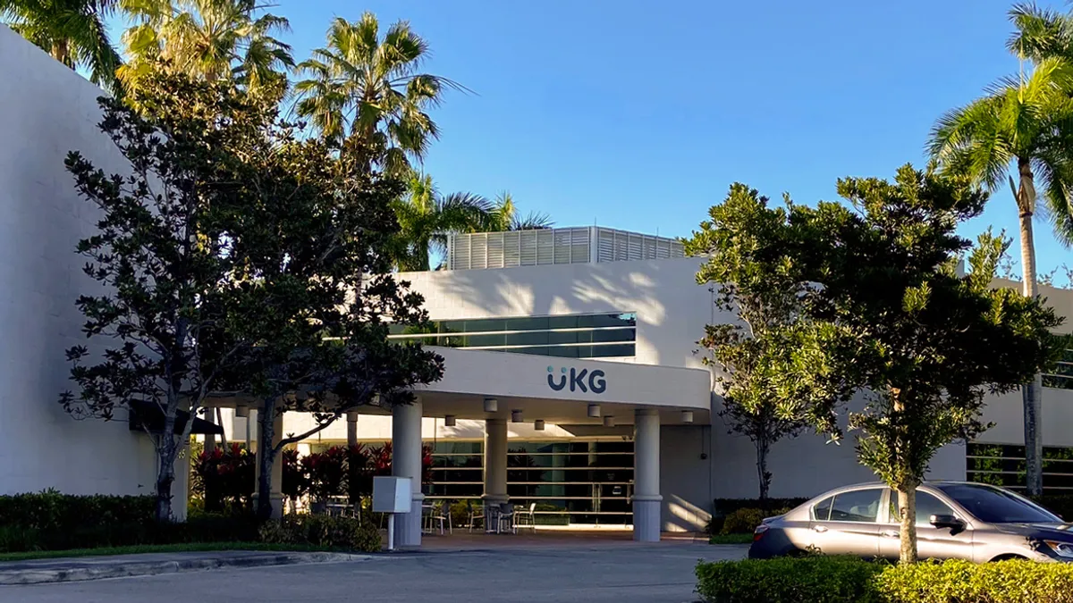 A building is seen from a parking lot with a sign that reads "UKG."