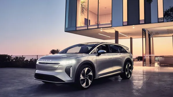 A silver Lucid Gravity electric SUV parked in front of a cantilevered building with blue sky in the background.