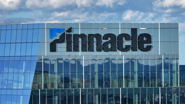 A glass office building with the word "Pinnacle" and its logo on the exterior is seen from high above Nashville's downtown.