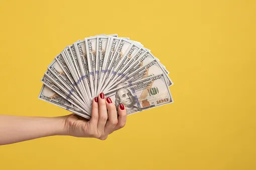 Hand holding money against a yellow background