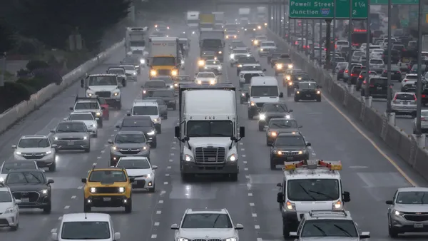 Several cars and trucks drive through a freeway on a semi-foggy day.