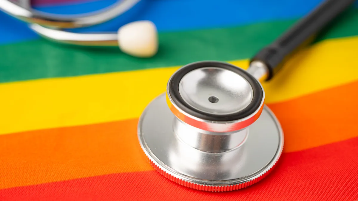 A black stethoscope rests diagonally on a rainbow flag background.