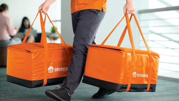 A man carrying orange bags with the word Grubhub on the side.