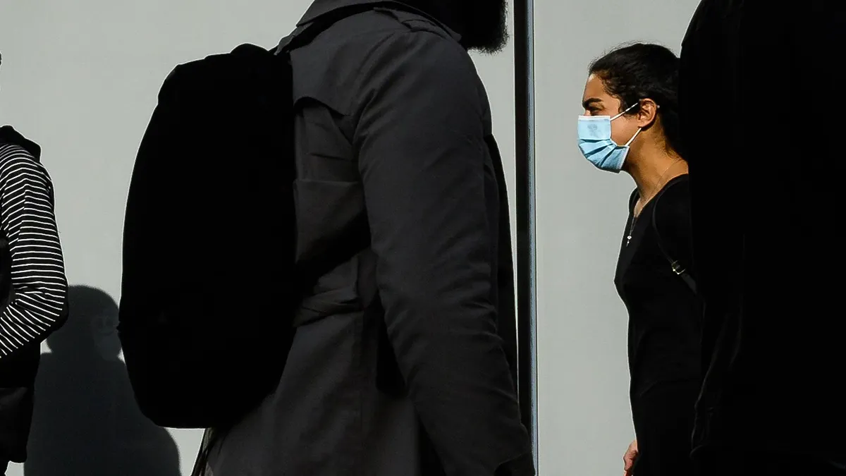 A woman wearing a protective facemask walks in the street, against other pedestrians' silhouettes