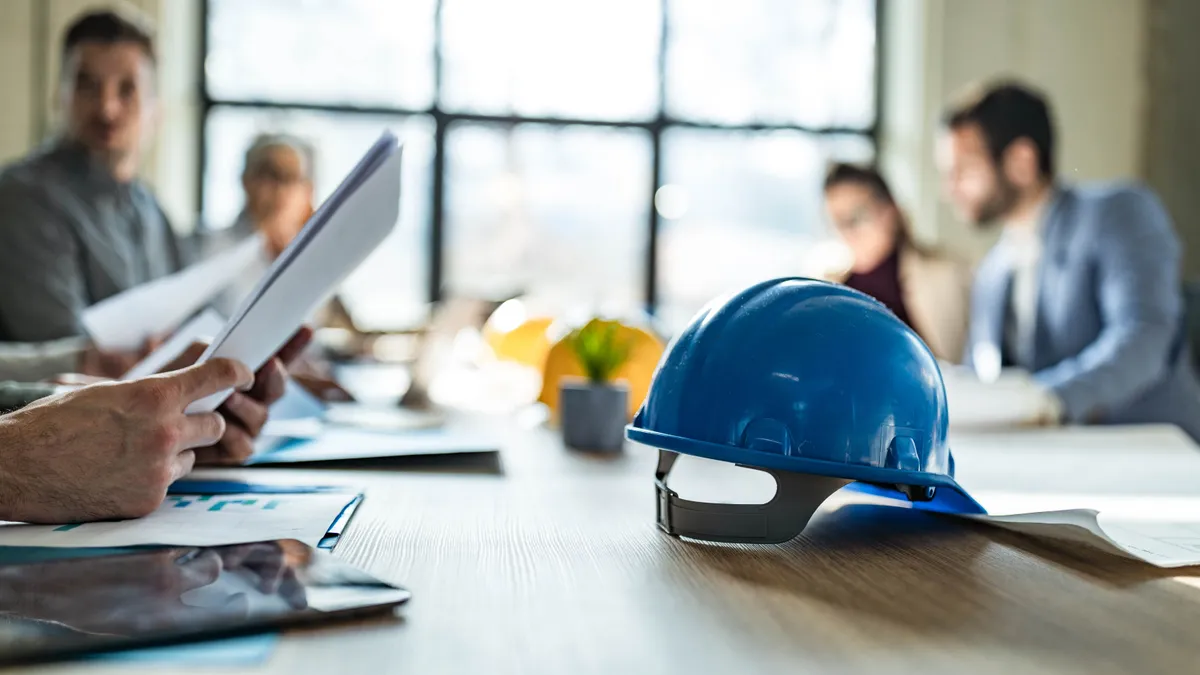 Close up of blue hard hat on a table during a business meeting in the office. Copy space.