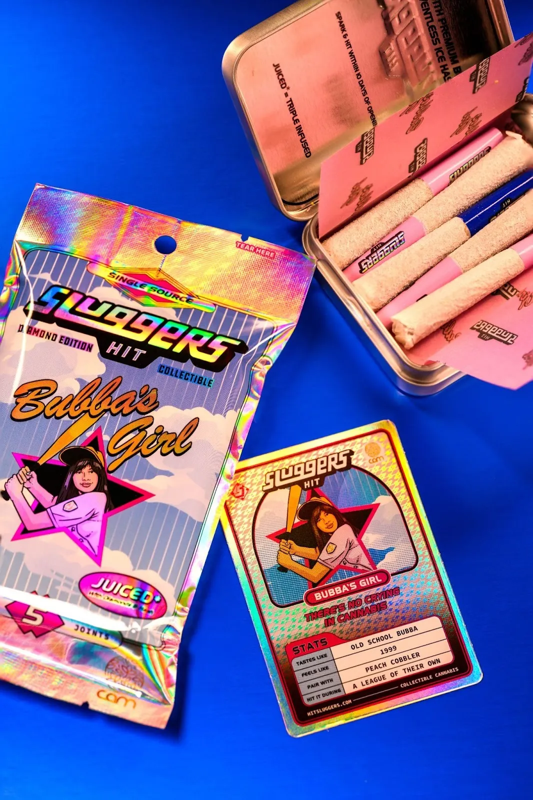 A pack that resembles baseball cards has Sluggers Hit cannabis branding and sits next to a tin with cannabis cigarettes.