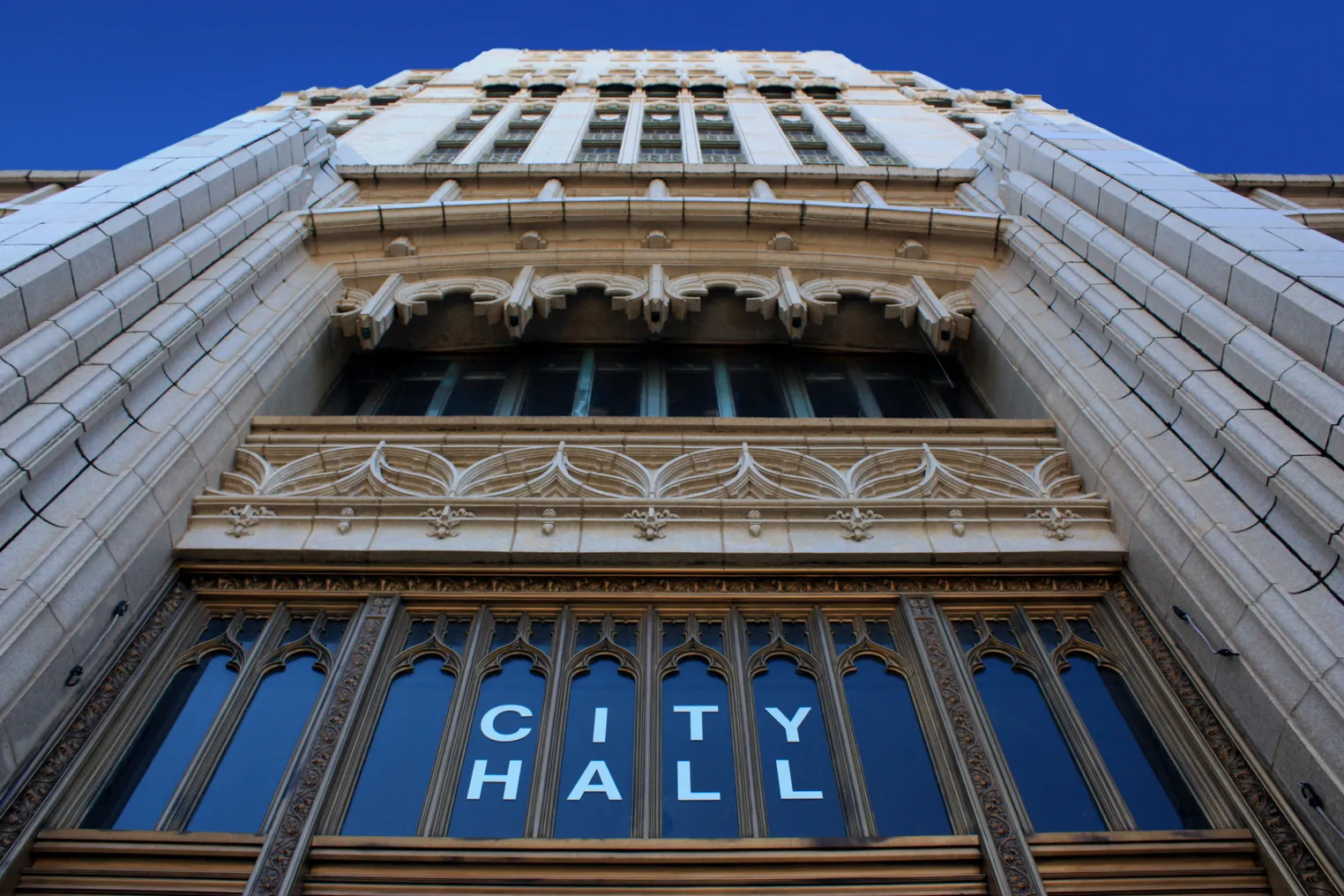 Shot looking up at the ornate facade of a building. Letters on the window read "City hall."