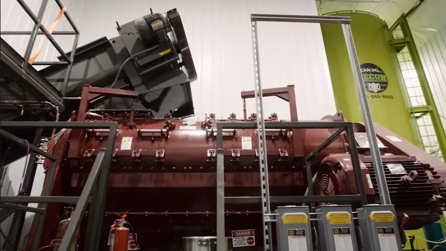 An industrial machine inside a building has a loading ramp and several turning components.