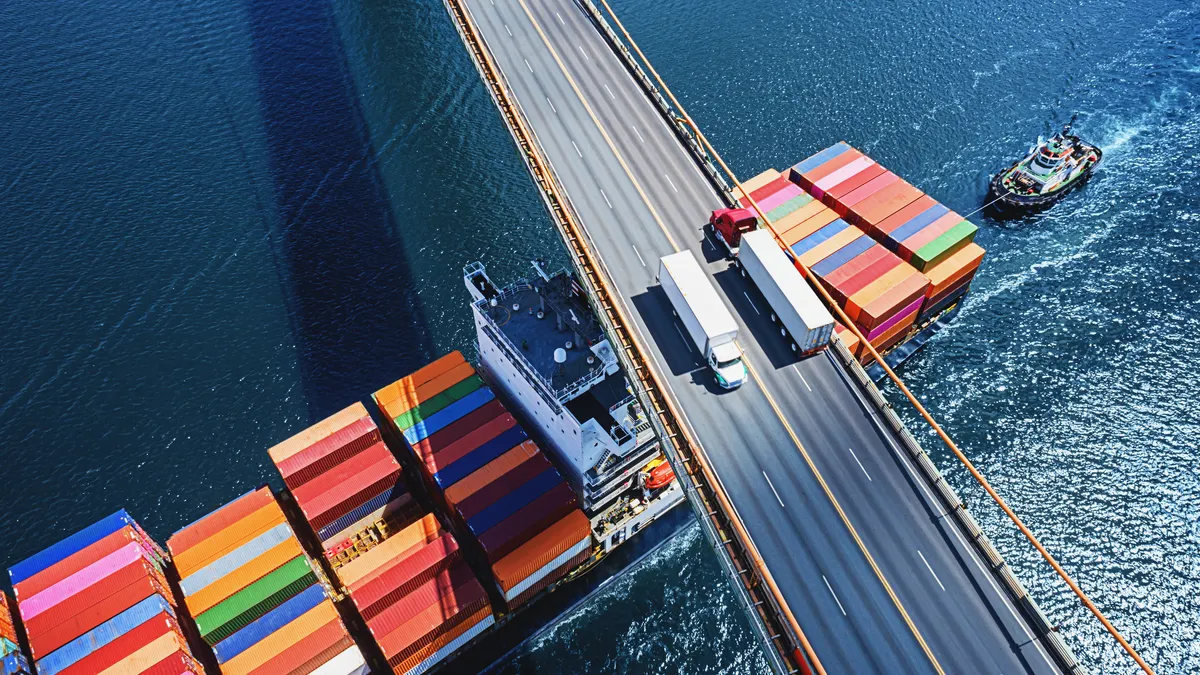 Trucks cross a bridge as a container ship passes underneath.