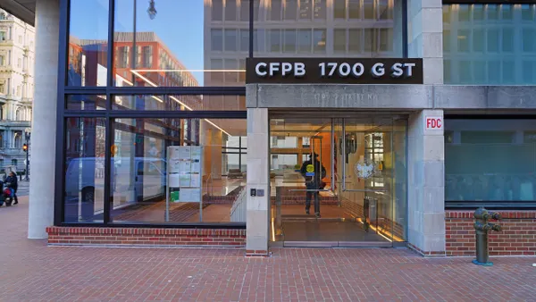 A modern cement and glass building with a sign that reads "CFPB 1700 G ST" is above a glass door entrance. 