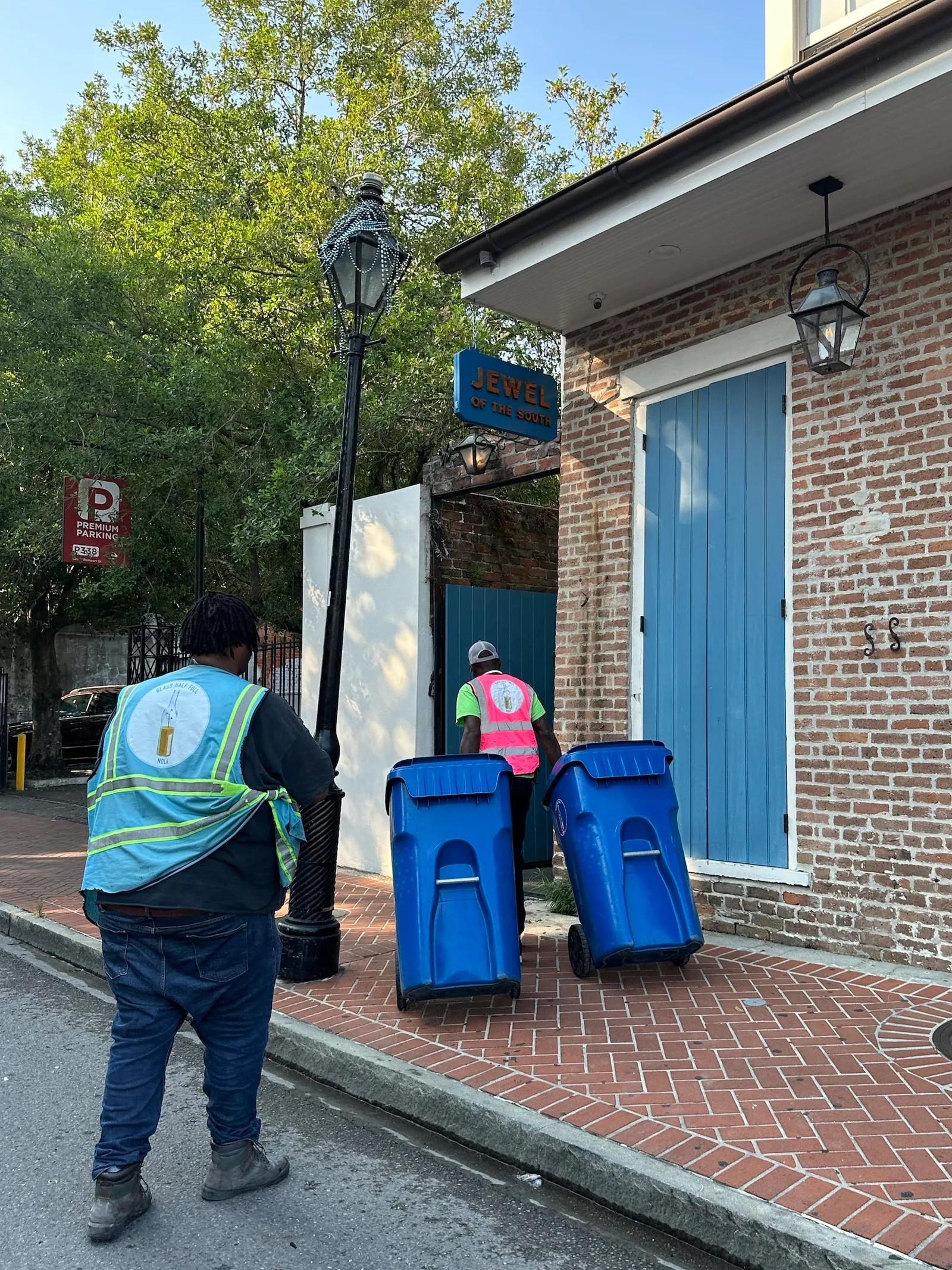 workers roll recycling bins along a sidewalk.