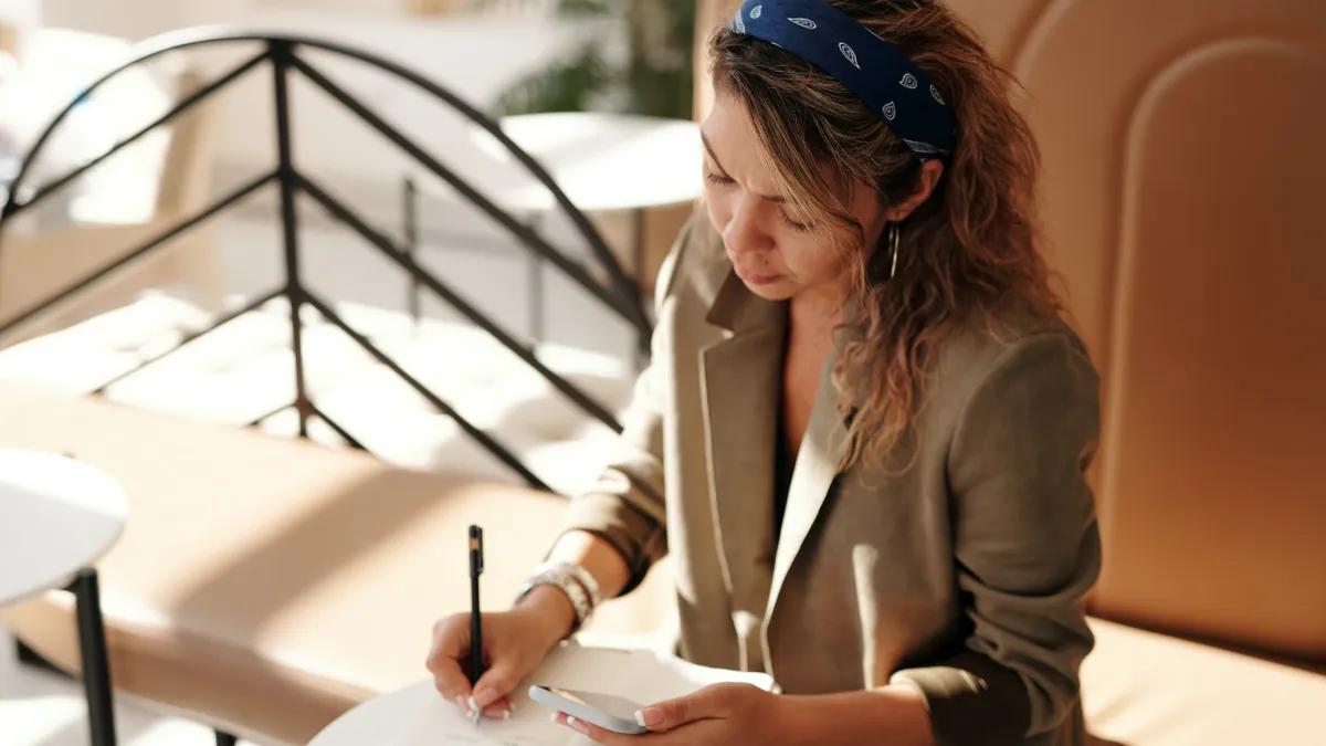 A woman of color reads documents and makes notes on them, with her head down