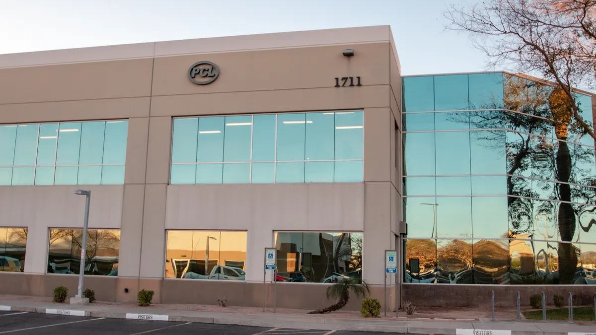 A gray stone building sits in the foreground, with a hint of asphalt in the front. The logo of PCL sits on the top right.