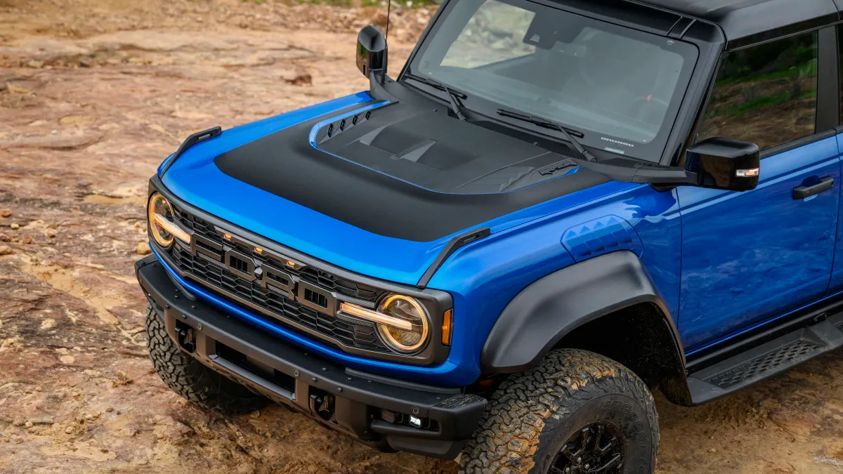 A view of the front half and hood of blue 2024 Ford Bronco Raptor from above with Black Appearance Package on a rocky trail outdoors.