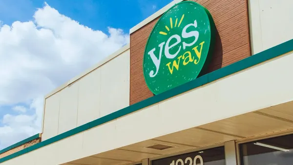 A ohiti of a green, yellow and white sign on the side of a building against a blue sky. The sign says Yesway.