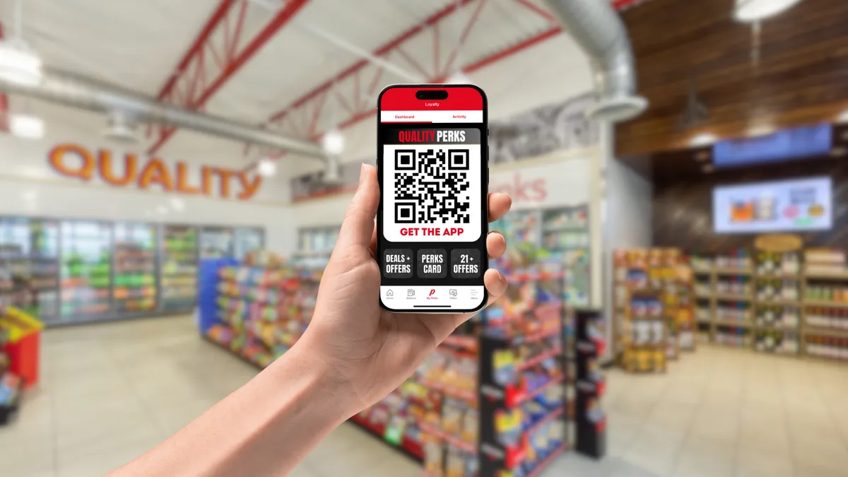 A photo of a hand holding a mobile phone that's showing a loyalty app on the screen. the screen reads "Quality Perks. Get the app. Deals + offers. Perks card. 21+ offers."