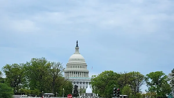 The Capitol Building in the background, with green trees on its left and right sides, and a water fountain in front of it.