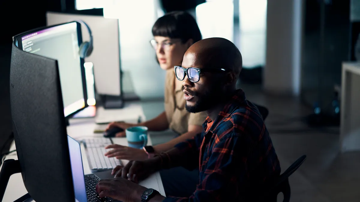 two software developers sit side by side in an office setting