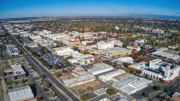 An aerial view of downtown Merced, California, during autumn with city buildings, trees and a blue sky in the background.