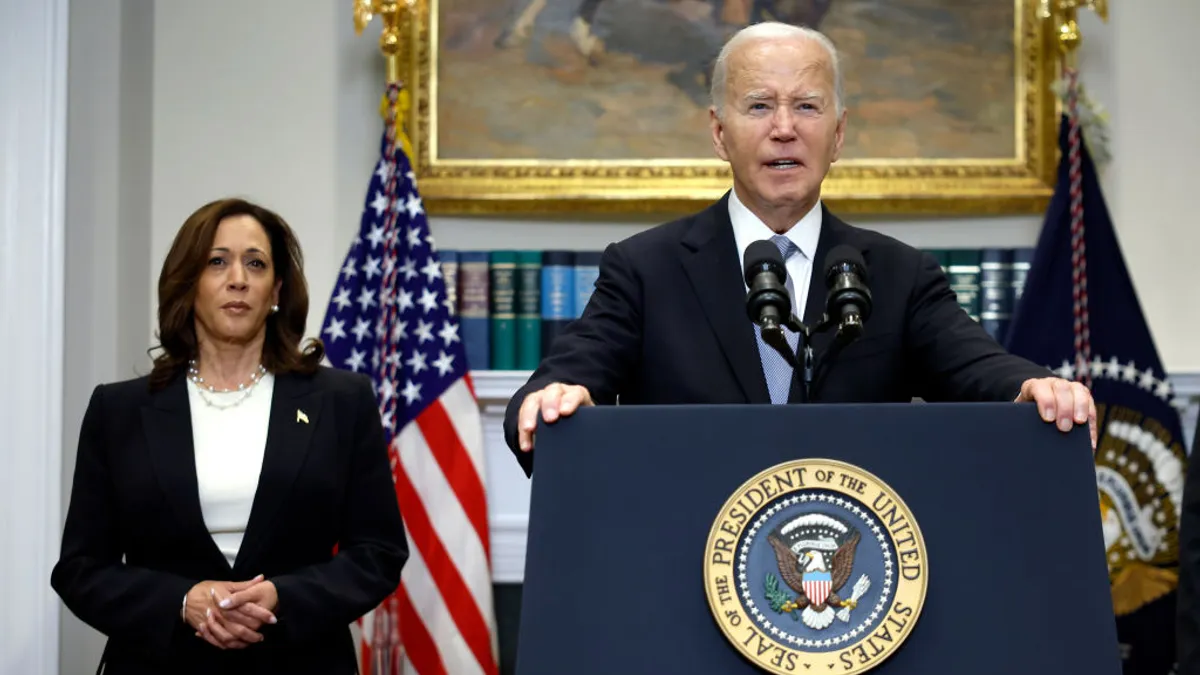 President Joe Biden delivers a speech at a podium while Vice President Kamala Harris stands in the background.