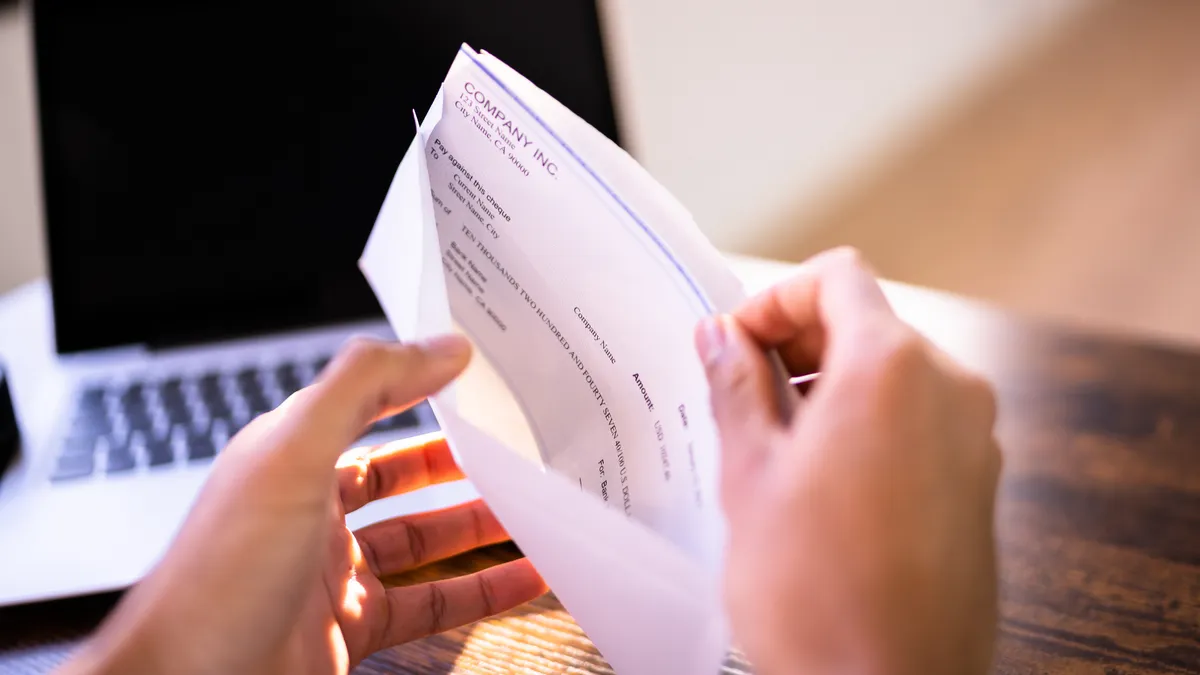 Hands holding a paycheck with a laptop in the background.