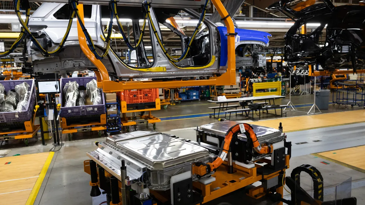 A unibody frame of a Jeep Grand Cherokee traveling down an assembly line above a battery cell.