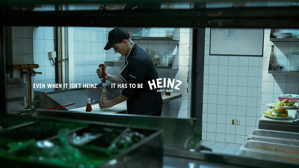 A restaurant worker wearing black fills up a bottle of ketchup.