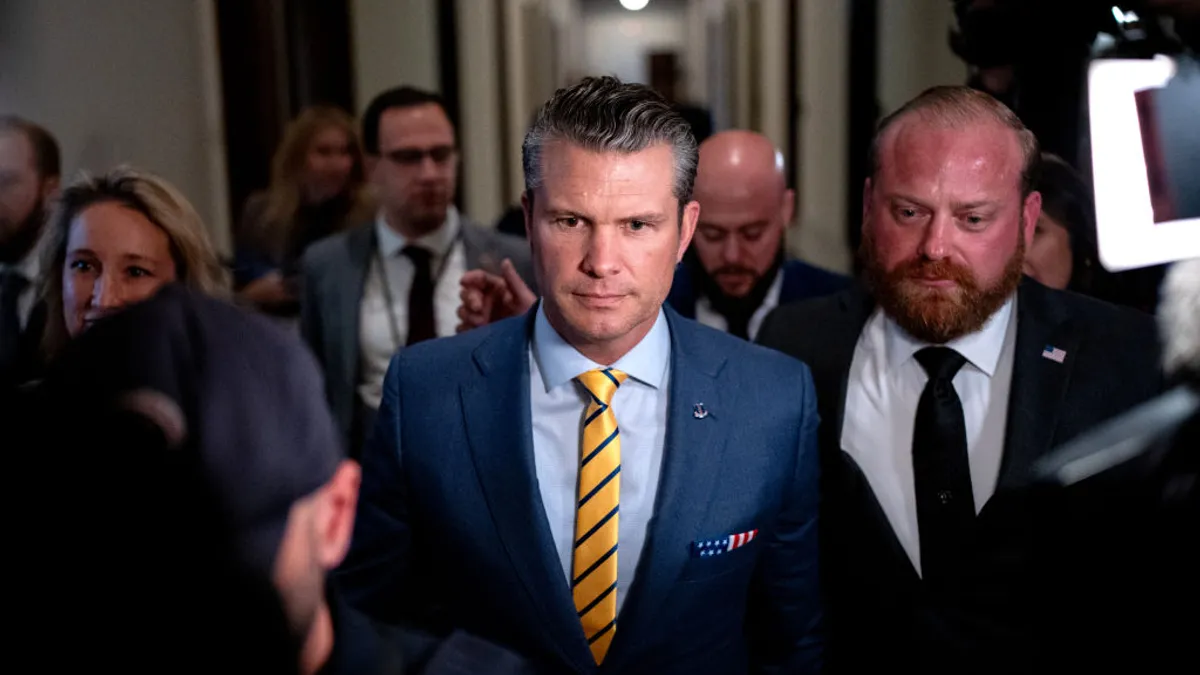 Man in blue suit and yellow tie walks through a crowded hallway