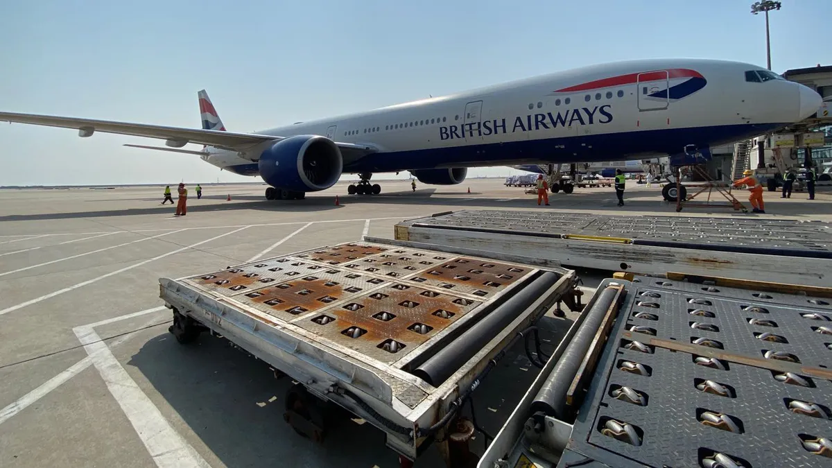 Cargo sits in front of a British Airways passenger aircraft on a tarmac.