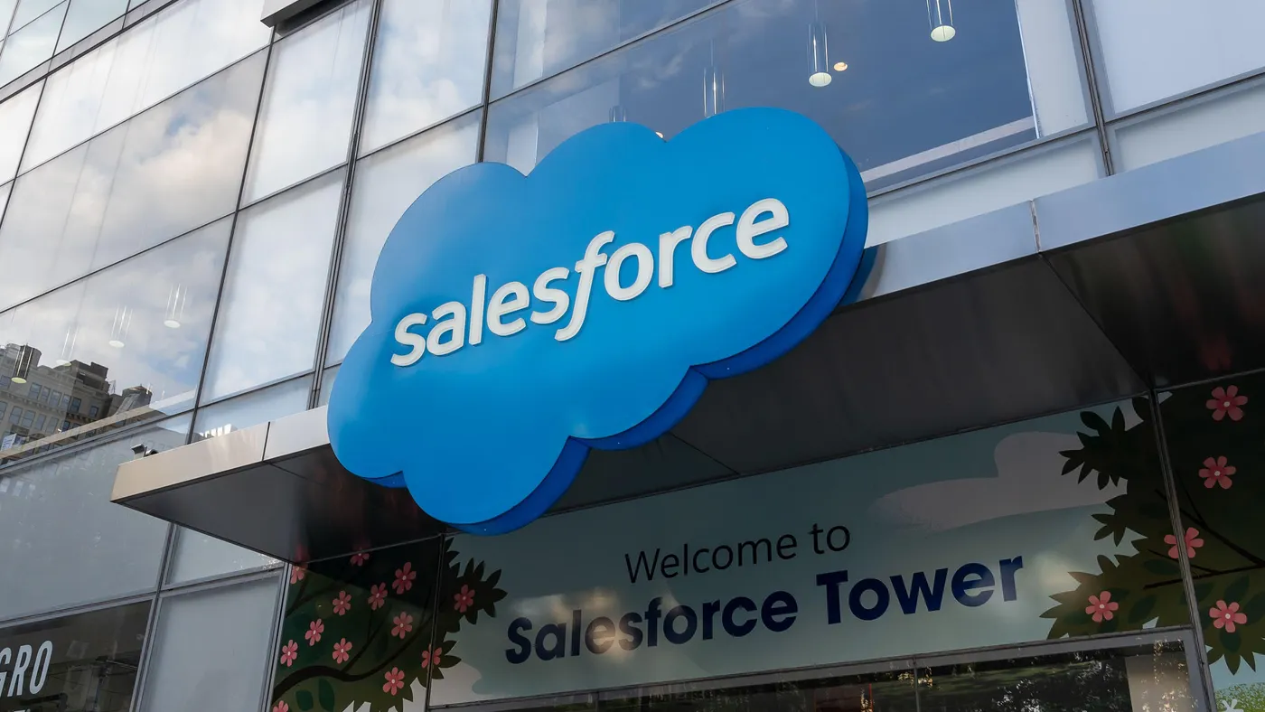 Entrance to a modern glass building with a large blue cloud-shaped sign that reads “salesforce.” The text “Welcome to Salesforce Tower” is displayed on the wall below the sign.