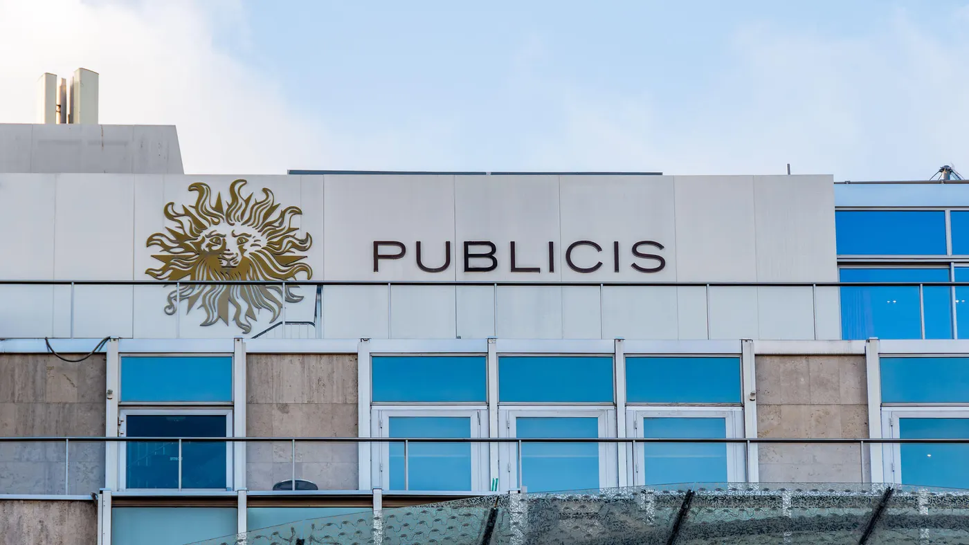 Building facade with large windows and a white panel displaying a golden lion logo next to the word “PUBLICIS” in thin capital letters.